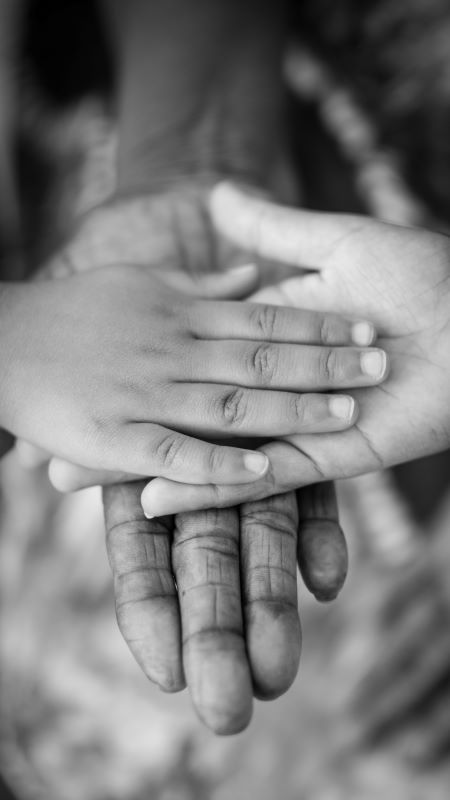 Grayscale hands layered together, from large adult hands at the bottom to a small child's hand on the top
