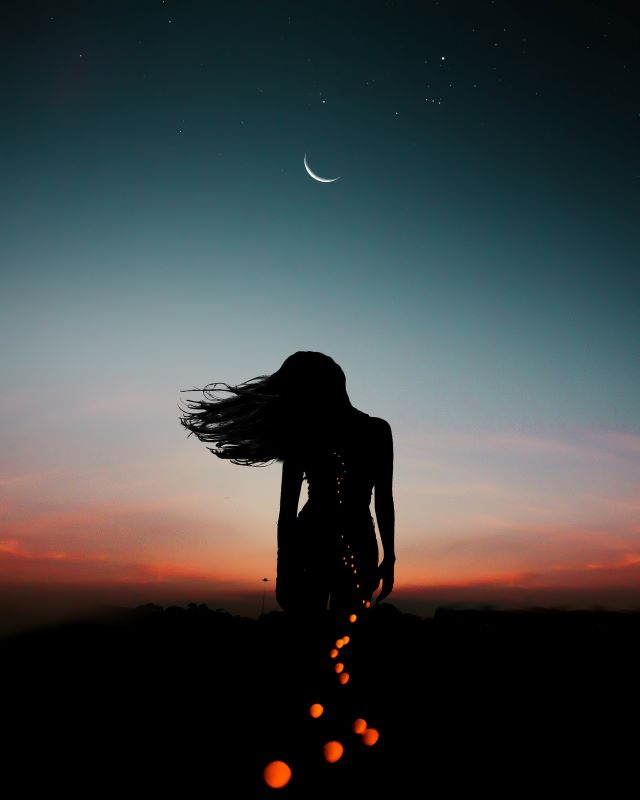 Woman standing in front of sunset and moon in sky