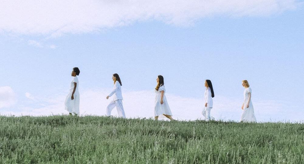 Women dressed in white walking in line along horizon