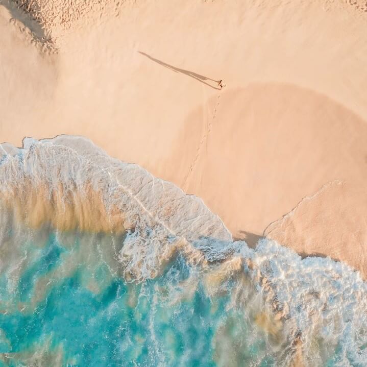 Aerial view of person walking on sand away from sea
