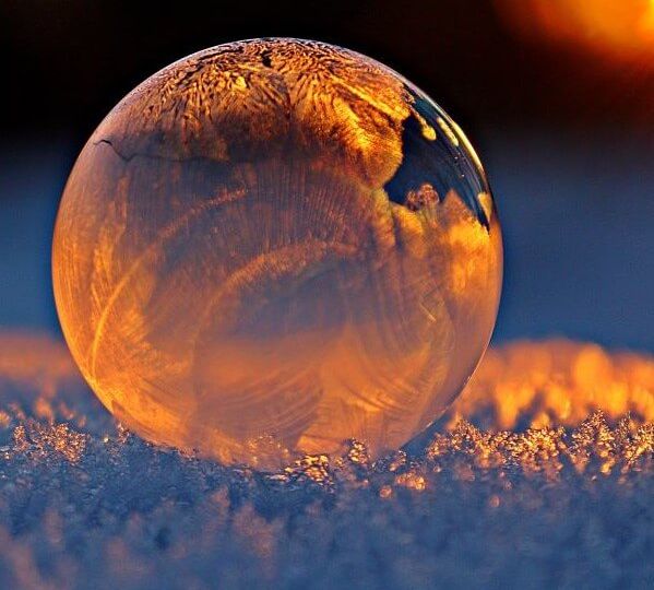 The snow on the ground appears blue-gray in the low light coming from the right side of the photo. A frozen bubble sitting on top of the snow fills most of the frame.