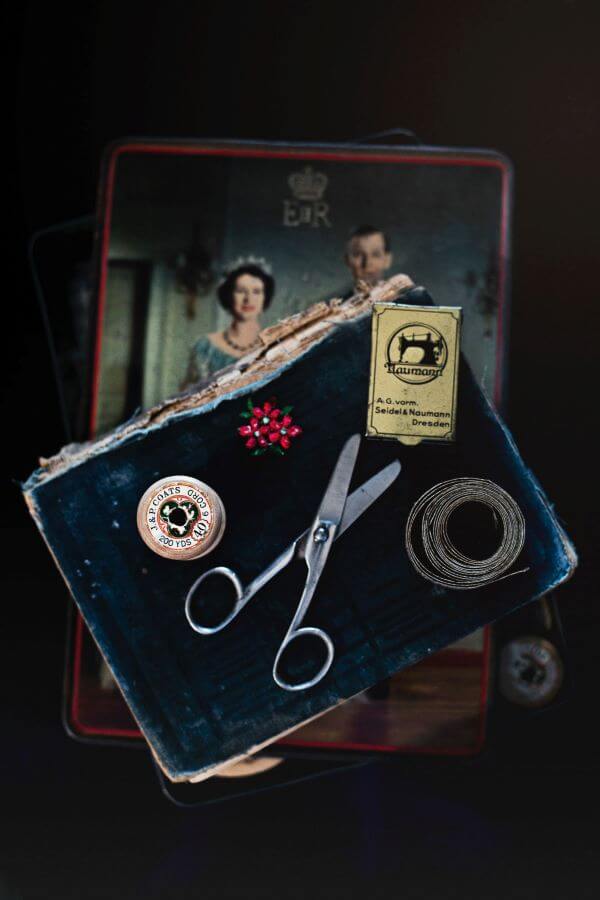 Seamstress tools, including shears, pins, and a tape measure sit on top of a book placed over a vintage pattern.