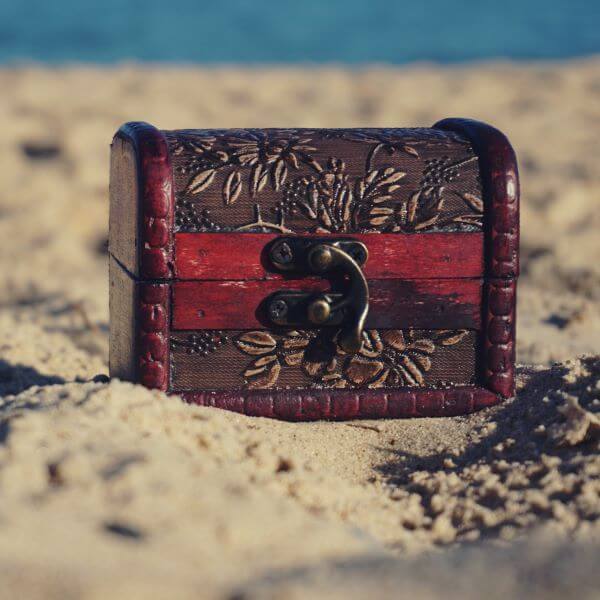 A small red wood chest with carved leaves sits on sand.